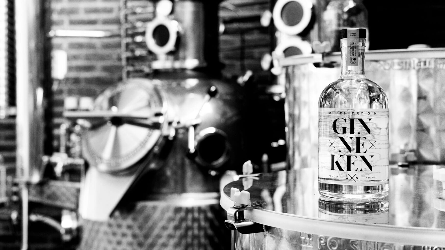 Bekijk een zwart-witfoto van een ginstokerij met een Gin Ne Ken-fles. Meer informatie op GinnekenGin.com.