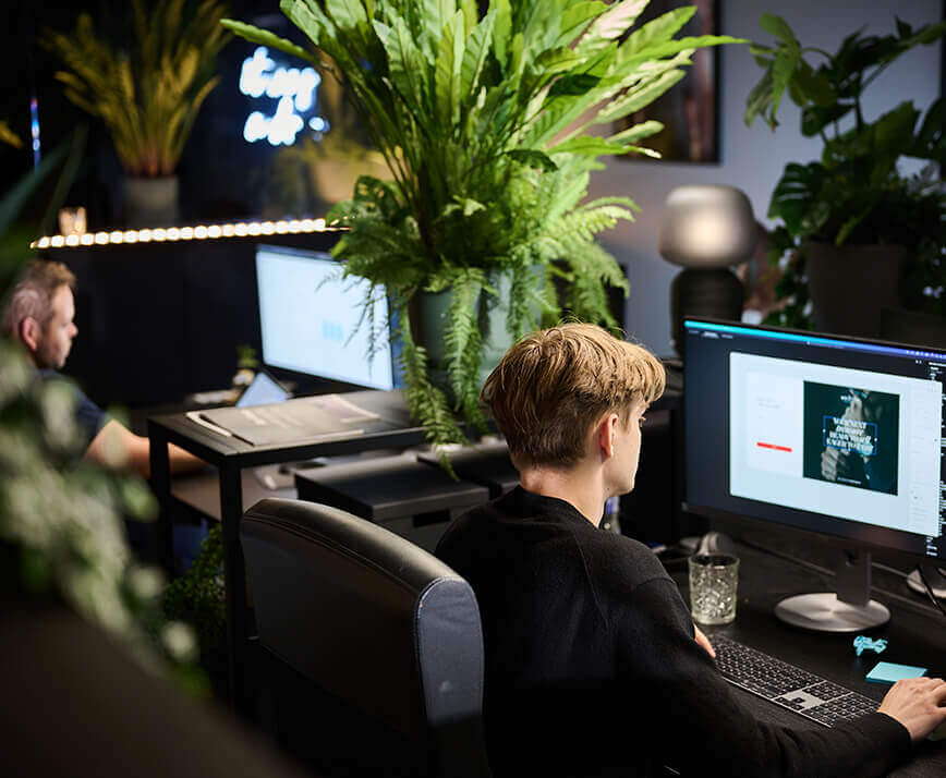 Werknemers achter computerbureaus, weelderige kamerplanten, moderne kantoorsfeer.