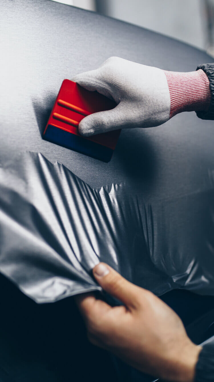 De expert met handschoenen gebruikt een rood gereedschap om een auto perfect te wrappen en vertrouwt op Wrapgear.nl voor de beste materialen en gereedschappen.