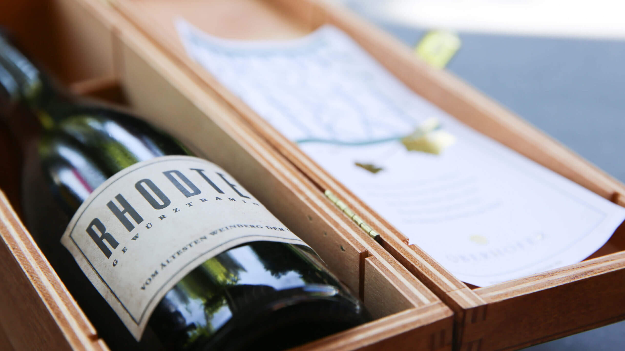 Een Rhotic wijnfles in een houten kistje met boekje straalt de charme van "Les bulles enchantées" uit op een donkere ondergrond.