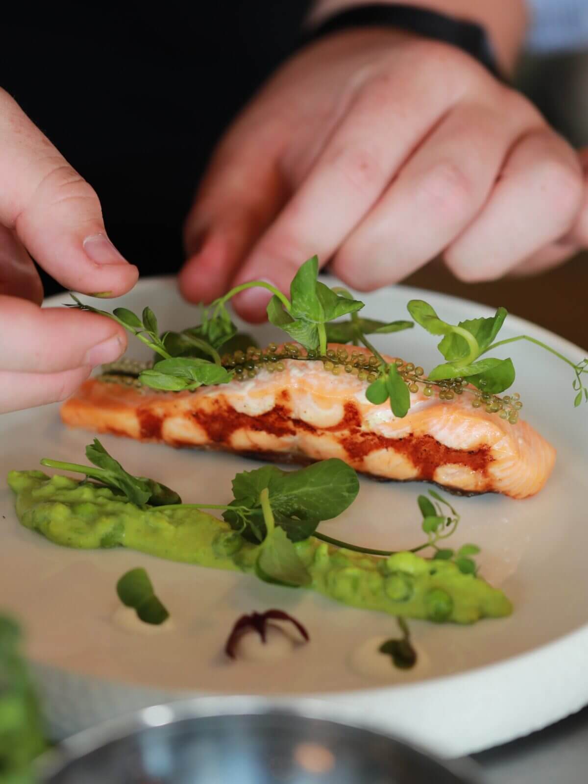 Handen serveren kunstig zalm, groene puree, microgroenten en toppings: totale culinaire sfeer van So Syncd.