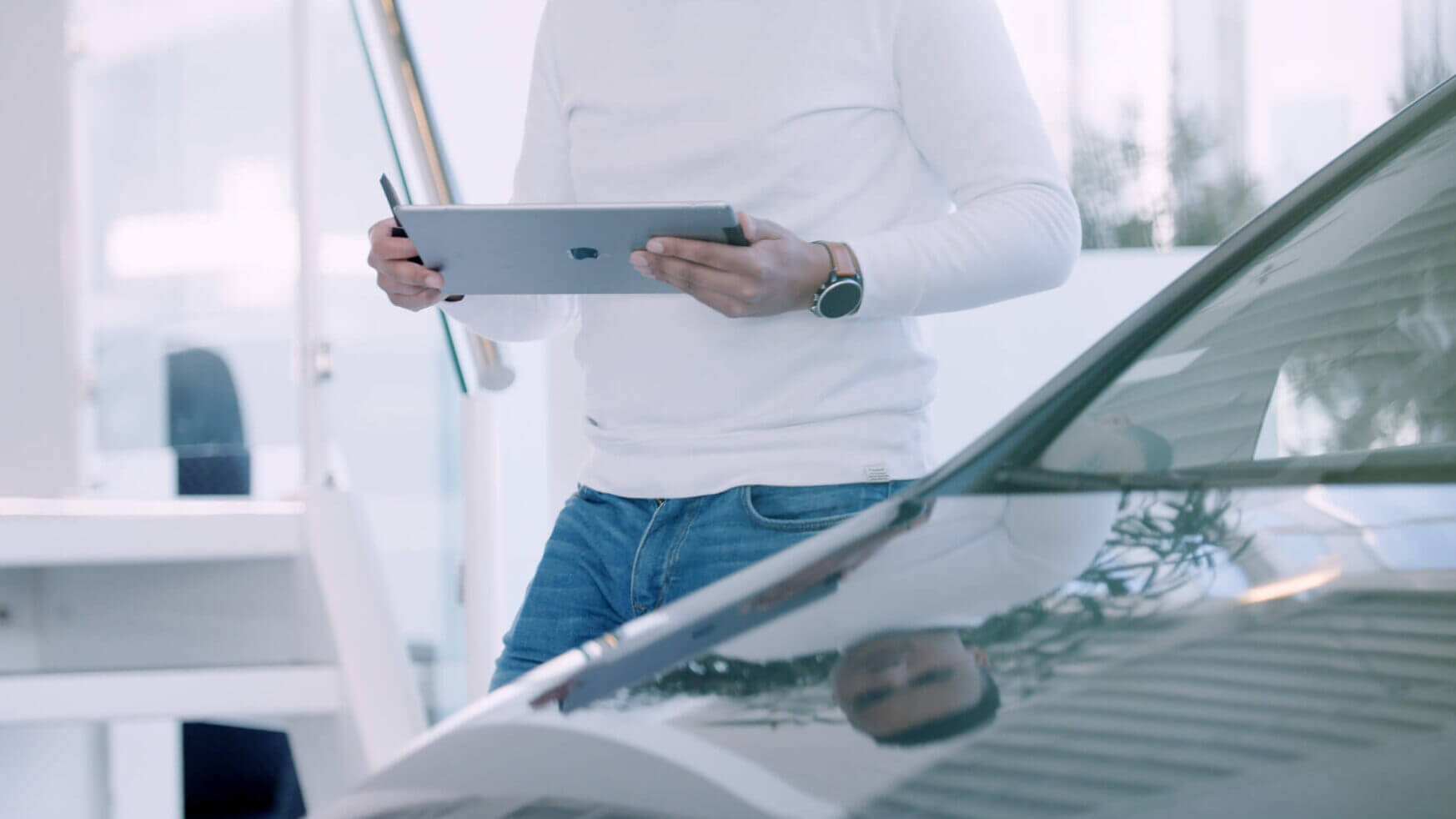 Op een helder verlicht kantoor gebruikt iemand in een wit overhemd de Car Collect-app op een tablet naast een auto.