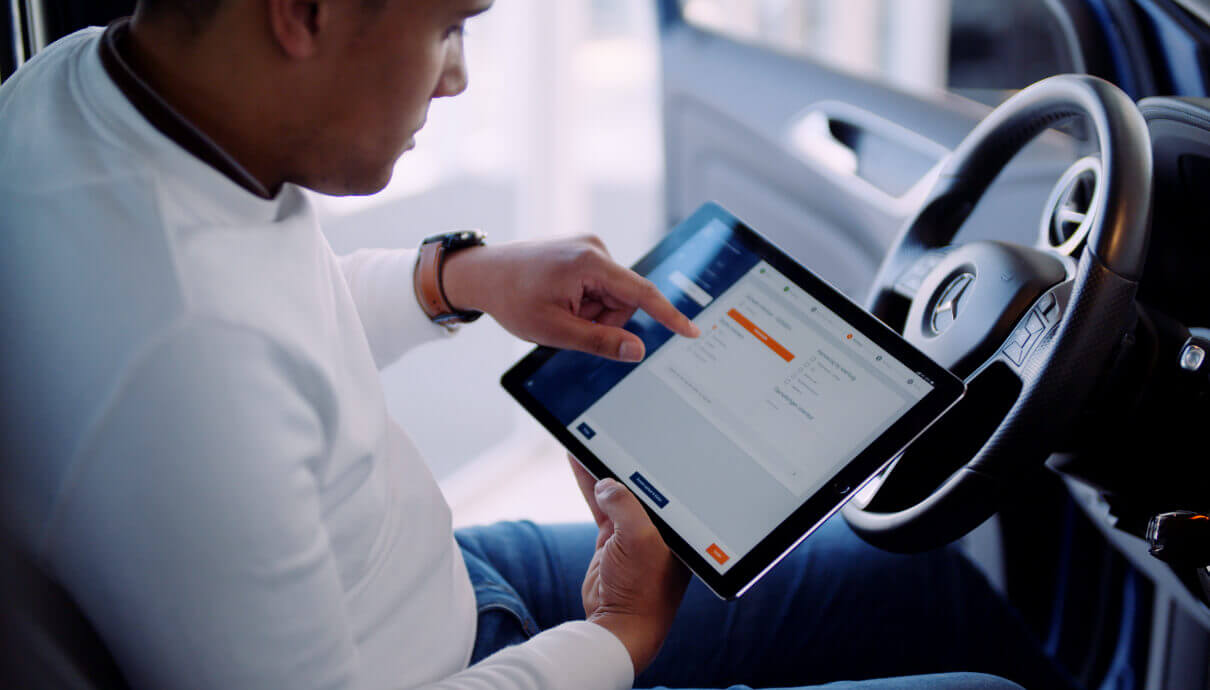 Een man zit in de auto en vult met behulp van Car Collect op zijn tablet nauwkeurig een digitaal formulier in.