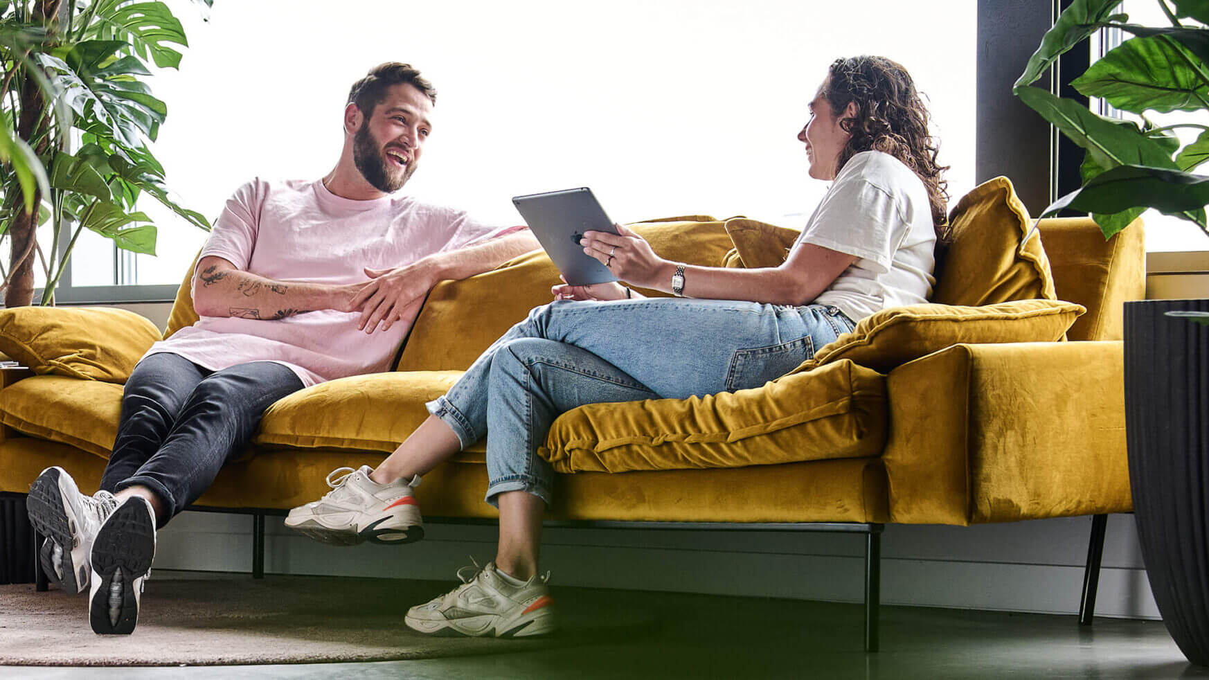 Twee mensen op een gele bank kletsen vrolijk en bespreken op een tablet strategieën voor leadgeneratie.