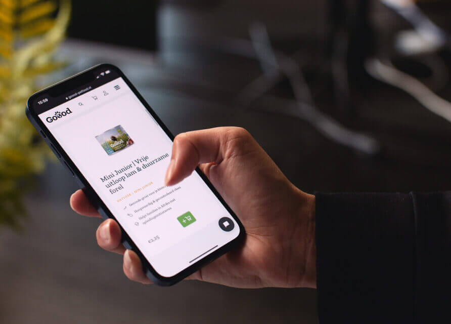 Iemand laat op zijn telefoon een GoFund-pagina zien, waarbij subtiel zijn merk wordt uitgelicht, tegen een onscherpe achtergrond van planten.