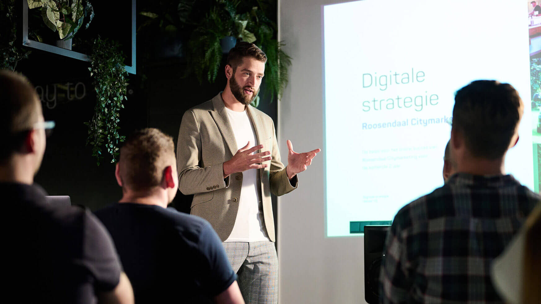 De presentator bespreekt digitale strategie en leadgeneratie aan een kleine groep in een donkere ruimte.