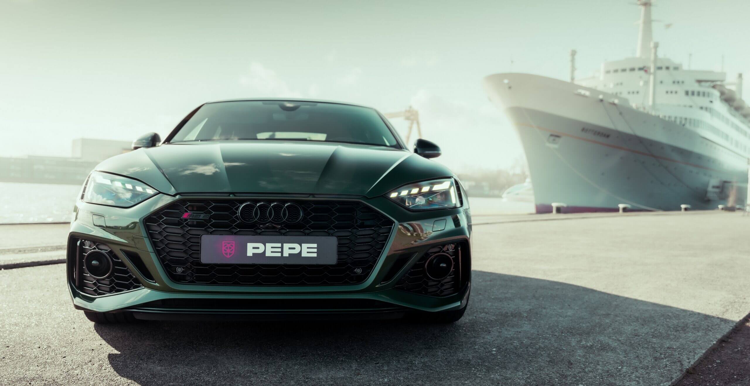 Groene Audi met PEPE-kenteken en Koppert Cress-sticker, geparkeerd naast een groot wit schip aan de kade.