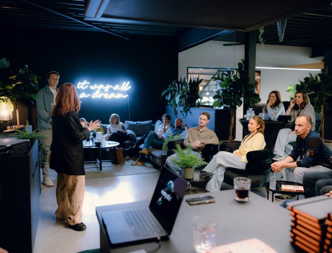 Vrouw presenteert Magento alternatieven aan een groep in een stijlvolle ruimte met neonlichten en planten.