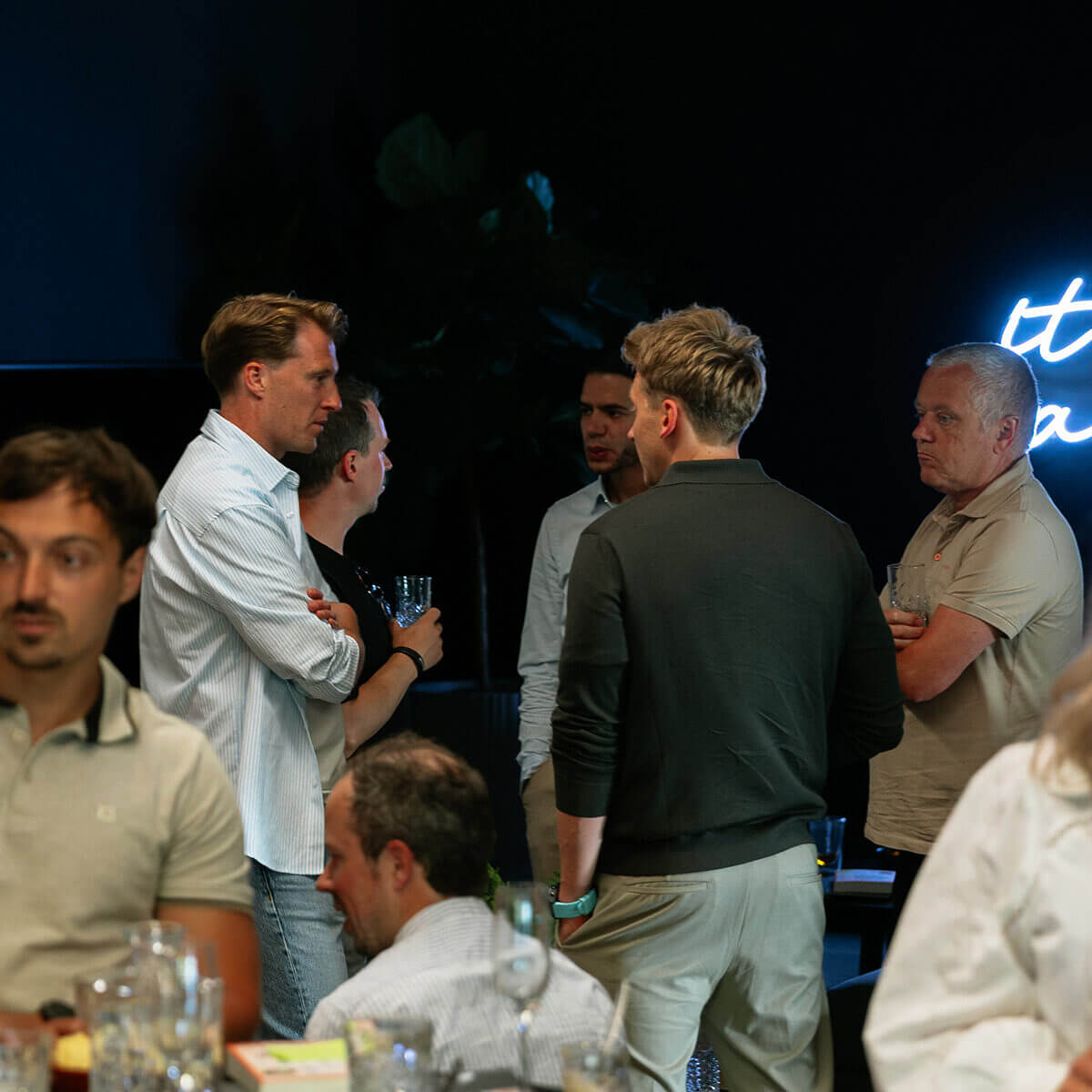 Mensen mengen zich met drankjes in de hand op een schemerig sociaal evenement.