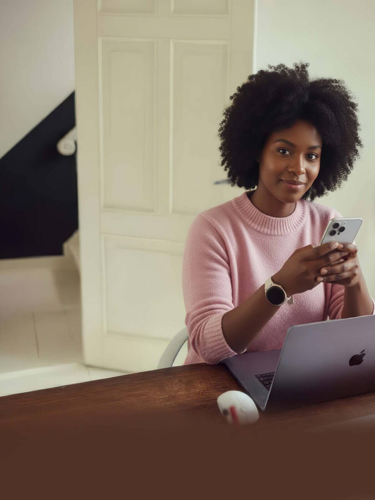 Glimlachende vrouw aan bureau met laptop en smartphone.