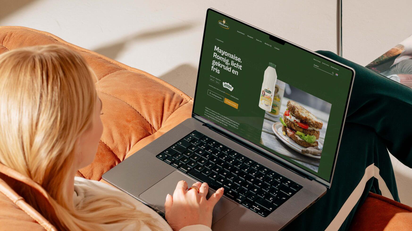 Persoon op een bank die met een laptop door een mayonaisewebsite bladert.