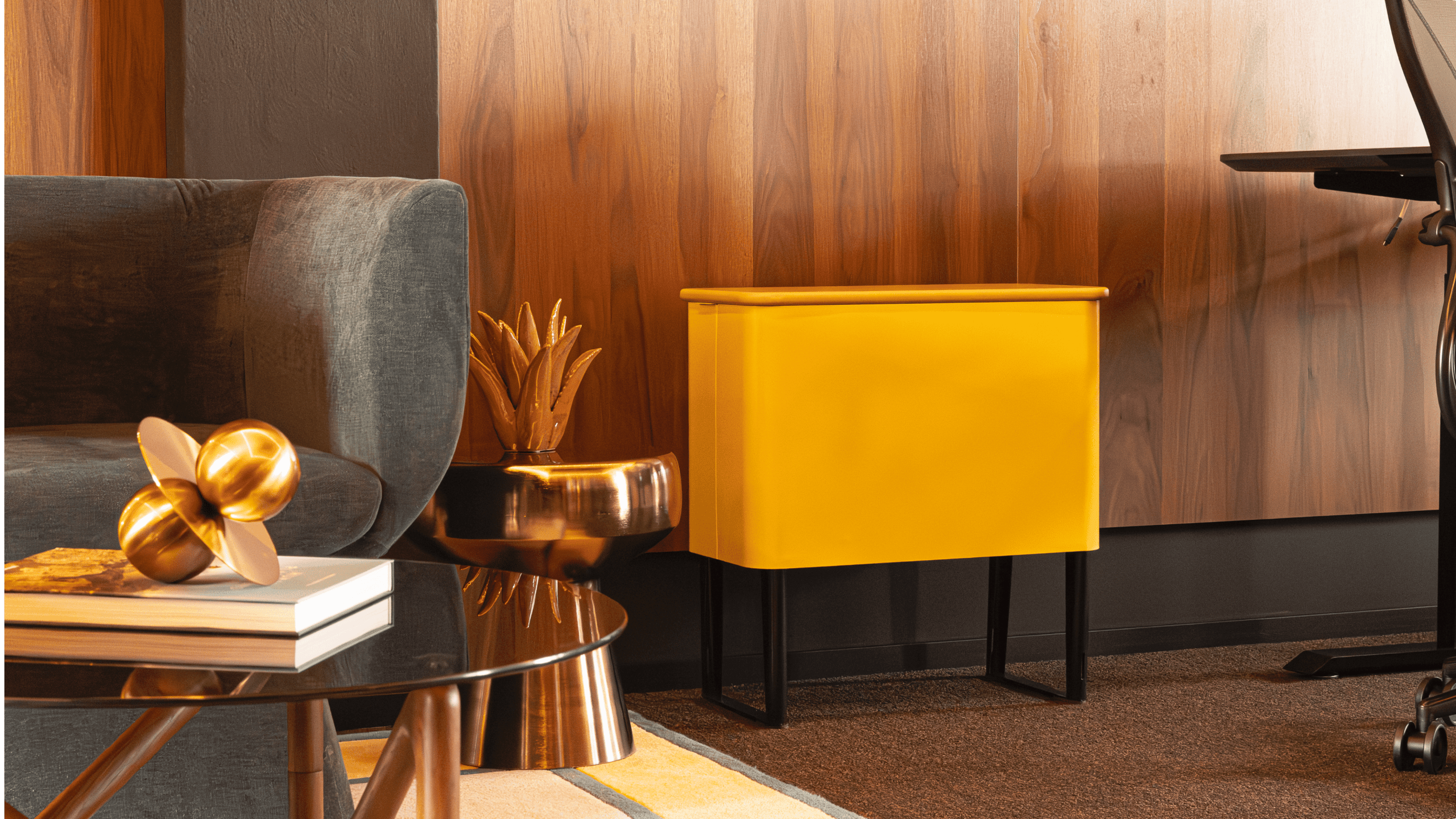 Moderne woonkamer met een gele bijzettafel, grijze bank en gouden accenten op een glazen salontafel.