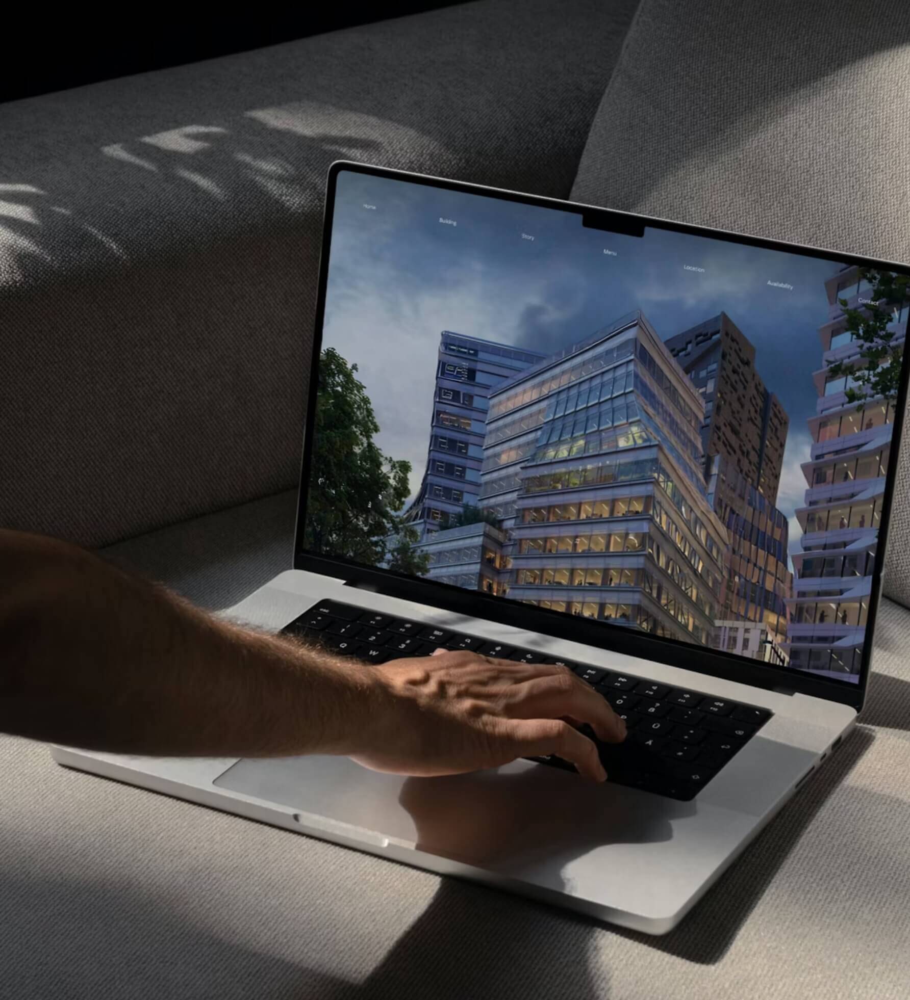 Persoon op een grijze bank die dagelijks een laptop gebruikt, modern gebouw getoond op het scherm.