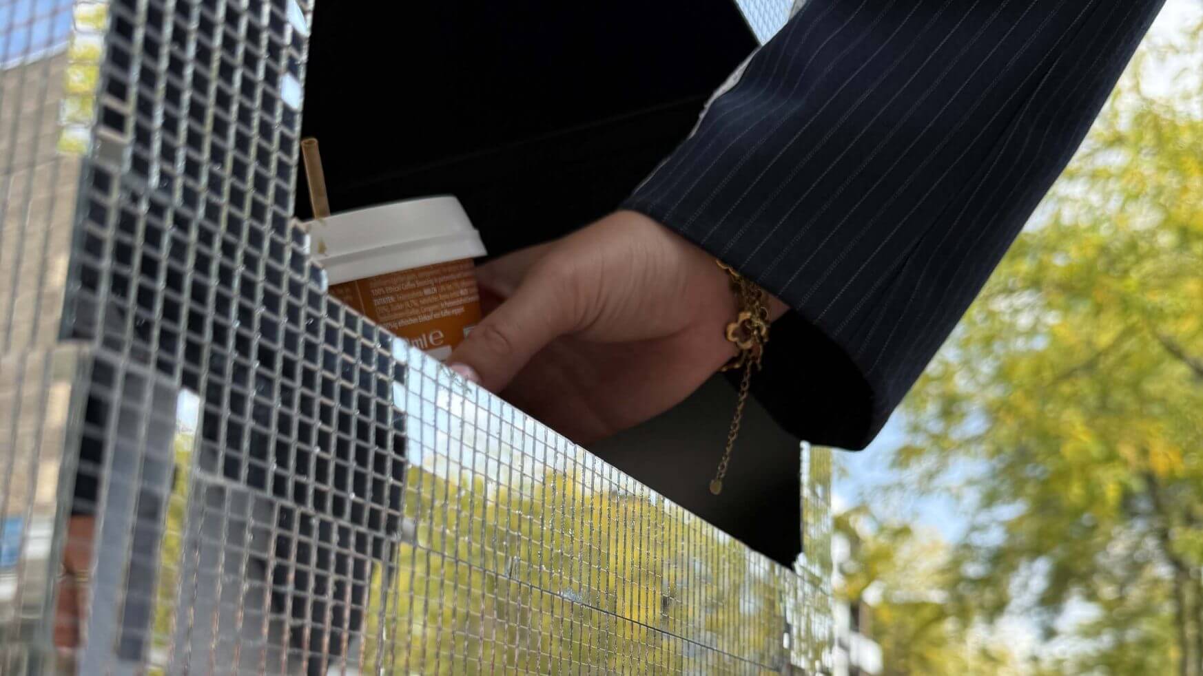 Hand in pak laat koffiekopje vallen in een glanzende doos met mozaïektegels buiten op een zonnige dag.