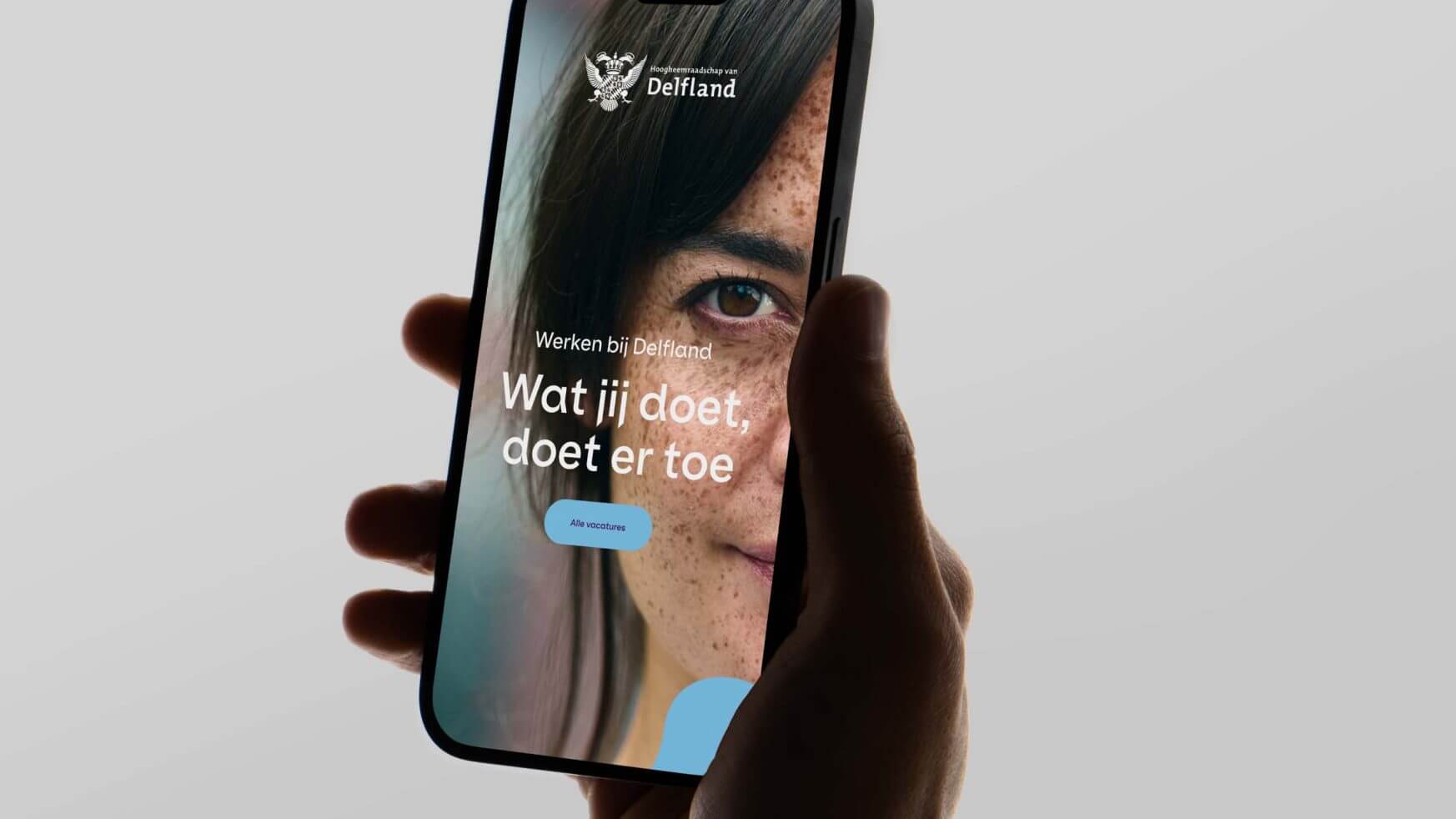 Hand die een telefoon vasthoudt waarop een website staat met het gezicht van een vrouw en Nederlandse tekst op het scherm.