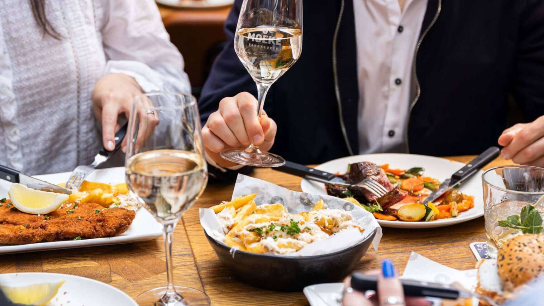Vier mensen delen wijn, friet en verschillende gerechten aan een restauranttafel.