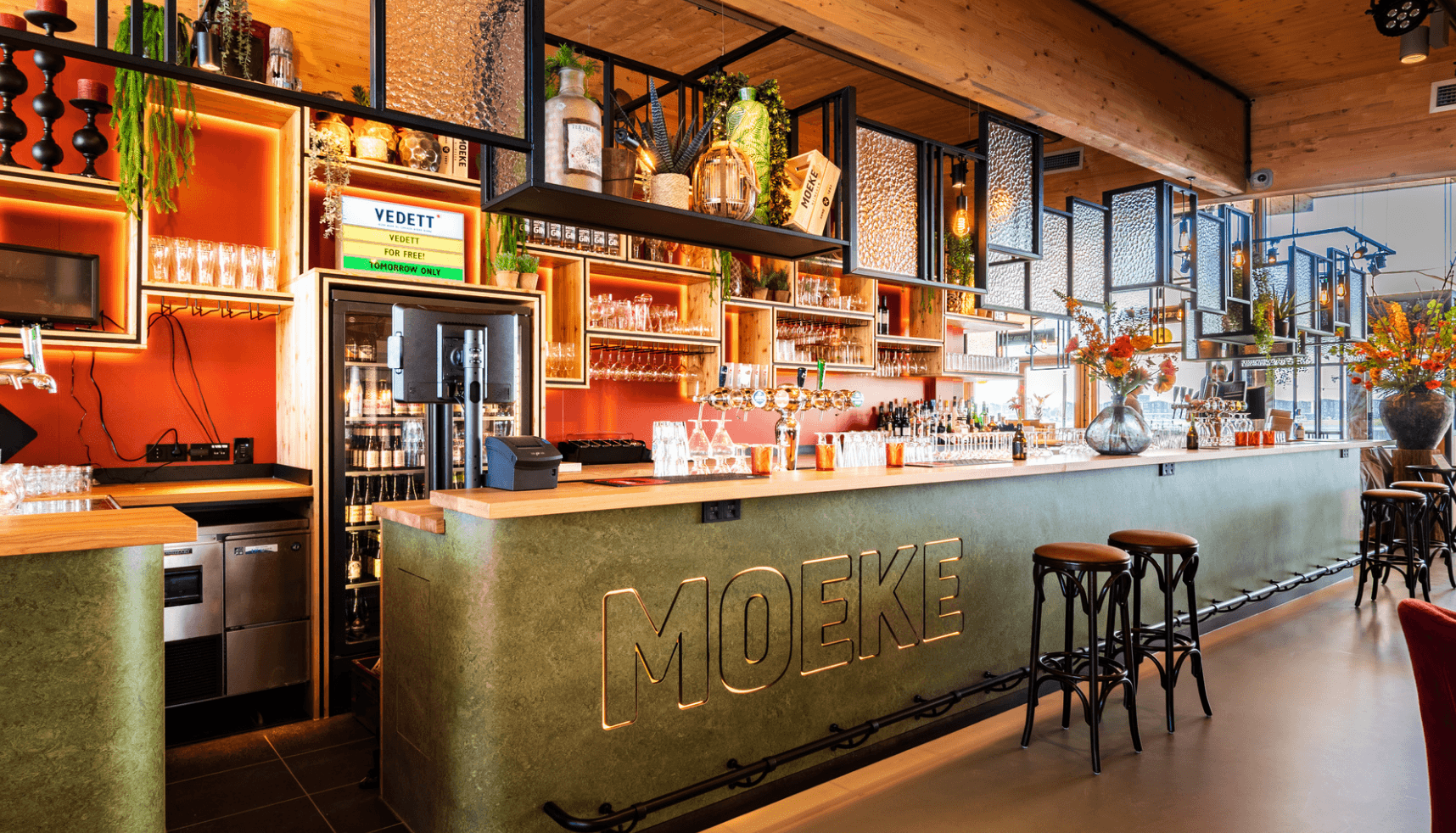 Chique bar met een groene MOEKE toonbank, planken met flessen en gezellige sfeerverlichting.