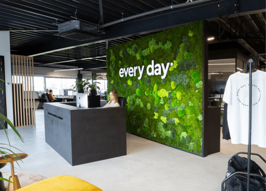 Moderne receptie met een groene mosmuur met de tekst "elke dag" en een persoon aan de balie.