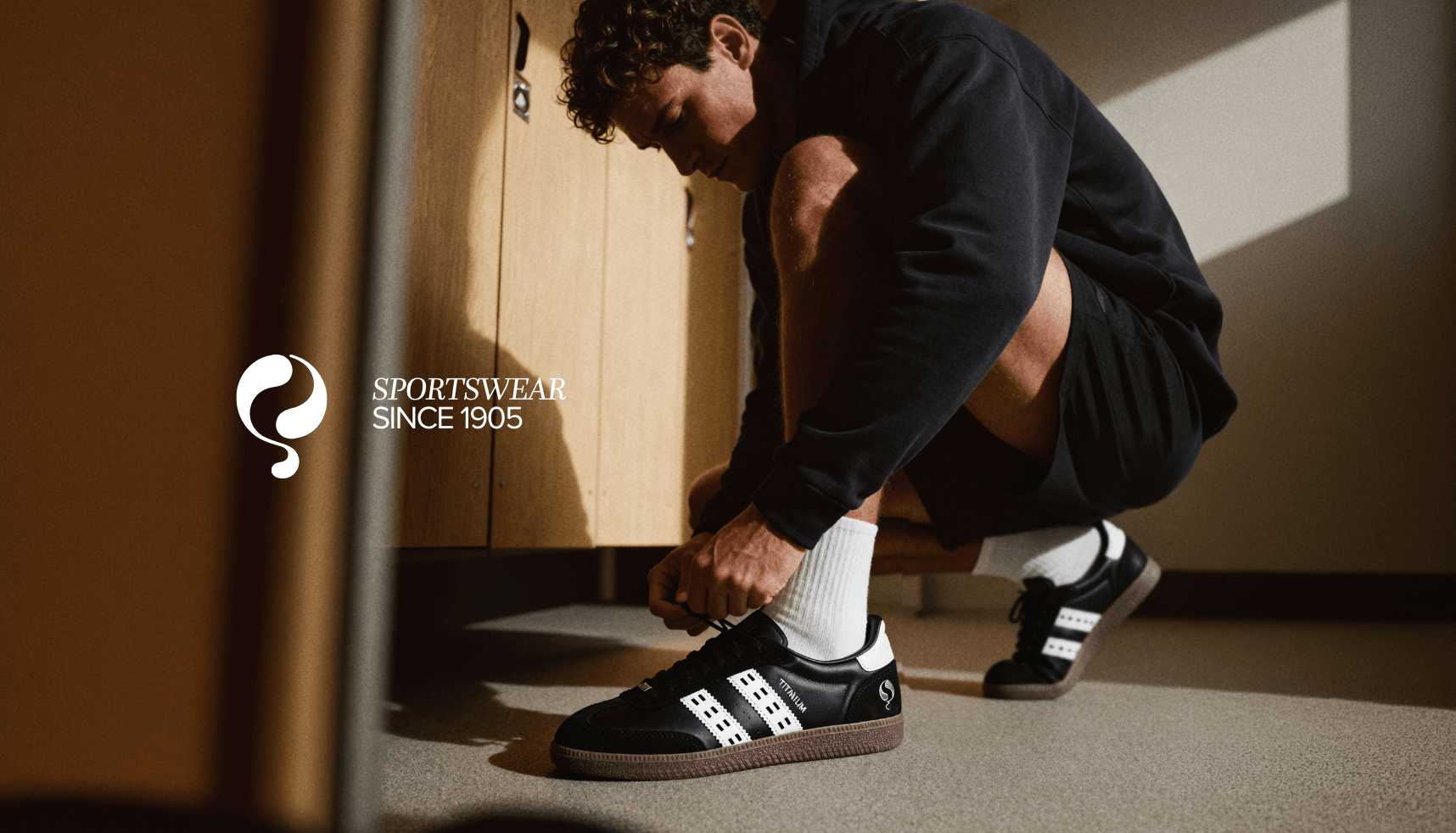 Atletische man knoopt zwarte gympen vast in een kleedkamer, met de tekst SPORTSWEAR SINCE 1905 en het merklogo zichtbaar.